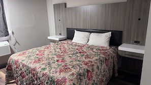 Ein Hotelzimmer mit einem Bett, Nachttischen, einem Fenster mit Vorhängen und einem an der Wand befestigten Regal.