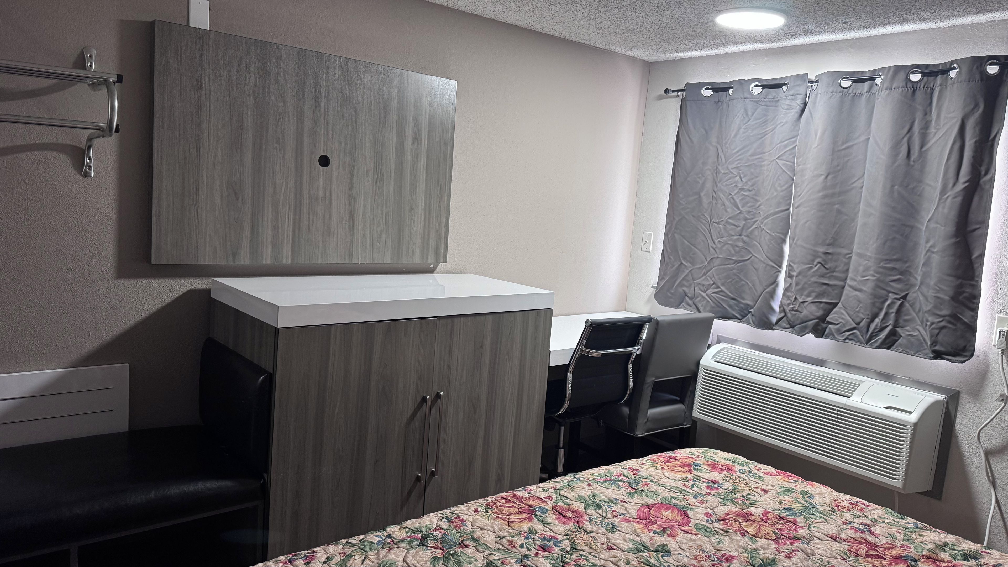 A bedroom with a bed, a desk, a wardrobe, a radiator, and a window with curtains.