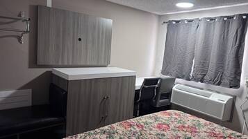 Ein Schlafzimmer mit Bett, Schreibtisch, Kleiderschrank, Heizkörper und einem Fenster mit Vorhängen.