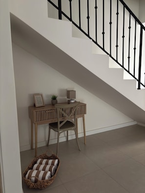 Eine Treppe mit schwarzen Stäben, ein Holztisch mit einem Stuhl, ein kleiner Tisch mit einer Pflanze und ein Korbkobold mit Handtüchern.