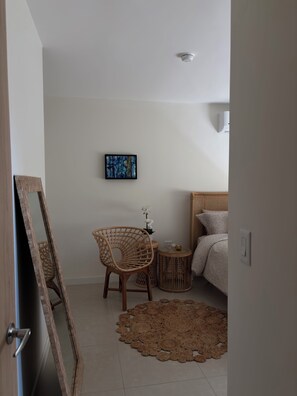 Ein Schlafzimmer mit einem Bett, einem Sessel, einem kleinen Tisch mit einer Orchidee, einem runden Teppich und einem Bild an der Wand.