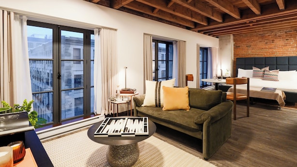 Una habitación de hotel moderna con techo de madera, ventanas amplias, un sofá, una cama y una mesa de centro.