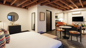 Una habitación de hotel con cama, escritorio, silla, televisor y una zona de cocina.