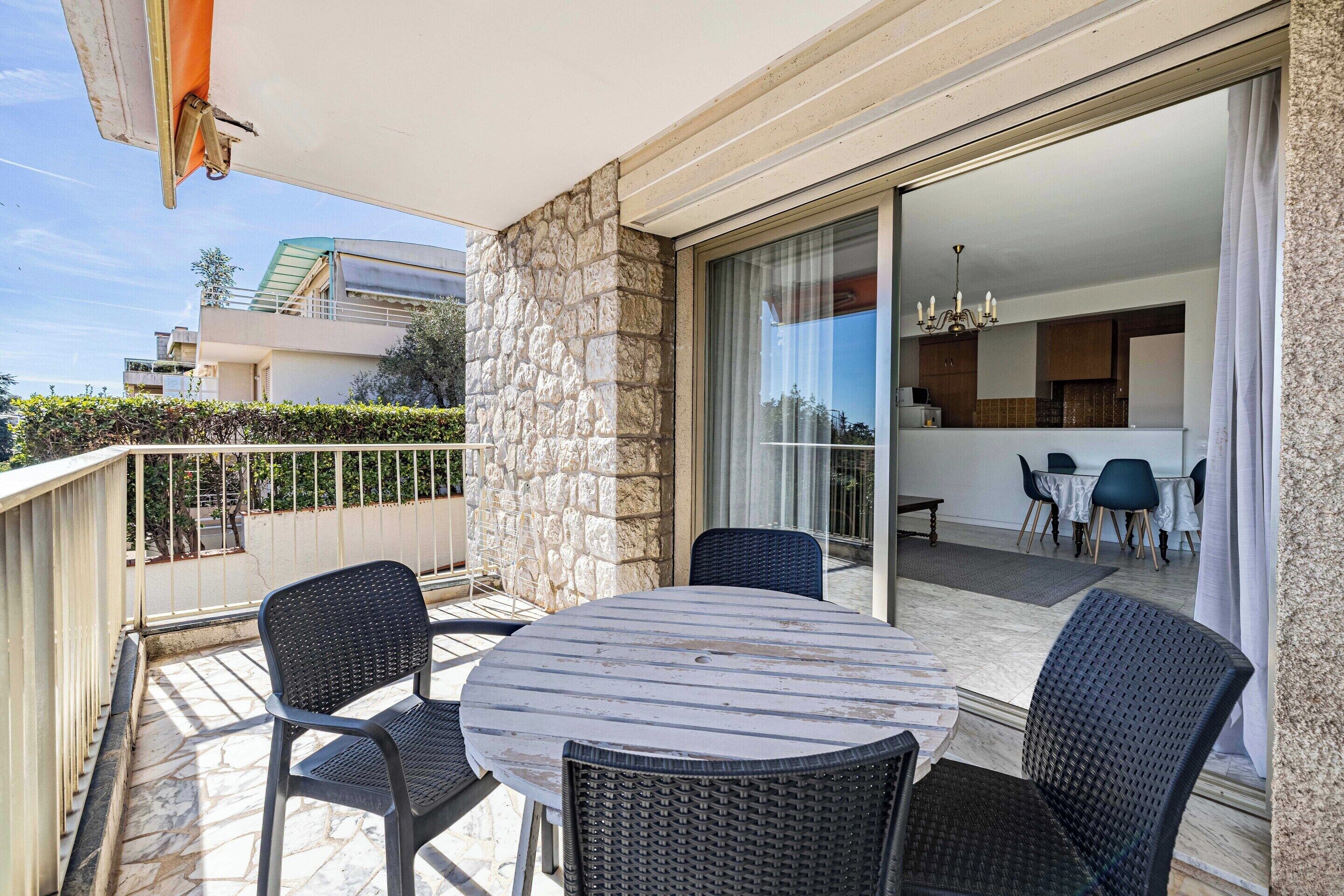 A balcony with a round table and chairs, a stone wall, and a view of a modern building.