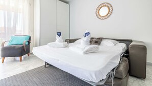 Habitación de hotel con cama, una silla, un sofá, un espejo y vistas al exterior.