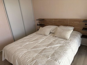 A neatly made bed with a quilted cover, a wooden headboard, and a bedside table with a lamp. - Seafront apartment in Erquy | 4 guests | Ref 506 (ERQUY)