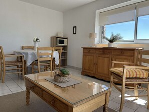 A dining area with a wooden table, chairs, a cabinet, and a television. - Seafront apartment in Erquy | 4 guests | Ref 506 (ERQUY)
