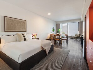 A hotel room with a large bed, a dining table with chairs, a TV, and a window with blinds. - Loft | Furnished Apartment Old Montreal, Quiet Courtyard, King Bed (Montréal)