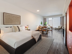 A hotel room with a large bed, a dining table with chairs, a TV, and a window with blinds. - Loft | Peaceful Apartment Old Montreal, Quiet Courtyard, Full Kitchen (Montréal)