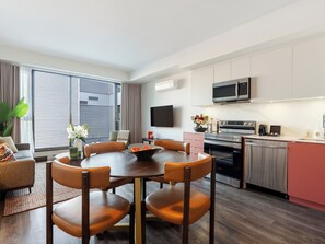A modern kitchen with a dining area, a flat-screen TV, and a large window with blinds. - Loft | Peaceful Apartment Old Montreal, Quiet Courtyard, Full Kitchen (Montréal)
