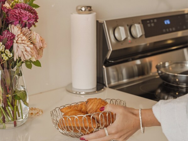 Keittiön työtasolla on maljakko täynnä kukkia, paperipyyhkerulla, kori täynnä croissant-leivoksia ja ruostumattomasta teräksestä valmistettu uuni.