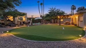 Un jardin bien entretenu avec un green d’entraînement au golf, un espace salon extérieur et une piscine.