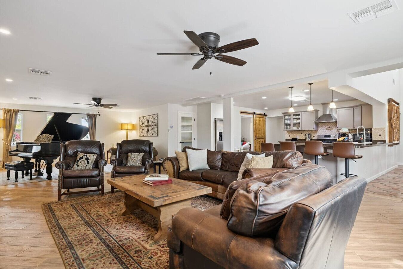 A spacious living room with a grand piano, leather sofas, a coffee table, and a ceiling fan.