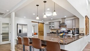 Une cuisine moderne dotée d’un îlot central, de tabourets de bar, d’appareils électroménagers en acier inoxydable et de luminaires suspendus.