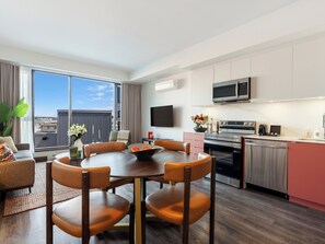 Een moderne hotelkamer met een eethoek, keuken en een groot raam met uitzicht op de stad.
