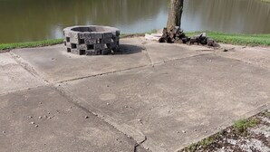 A concrete fire pit area near a lake with a pile of firewood. - Tranquility surrounds this house. View includes Three Lakes &  Quiet wilderness. (Jeannette)