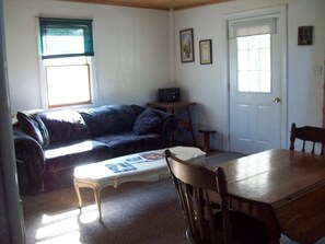 A living room with a dark-colored sofa, a wooden dining table, and a small side table. - Tranquility surrounds this house. View includes Three Lakes &  Quiet wilderness. (Jeannette)