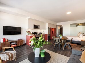 A modern living room with a flat-screen TV, a dining area with a table and chairs, a kitchen with a microwave and stove, and a separate bedroom with a bed and a mirror. - Loft with Balcony | Boutique Apartment Old Montreal, Courtyard, Full Kitche (Montréal)