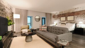 A modern hotel room with a flat-screen TV, a sofa, a coffee table, a bed, and a brick wall. - Two-Bedroom Suite | Private Apartment Old Montreal, Quiet Retreat, King Bed (Montréal)