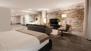 A modern hotel room with a large bed, a sofa, a TV, and a stone wall. - Two-Bedroom Suite | Private Apartment Old Montreal, Quiet Retreat, King Bed (Montréal)