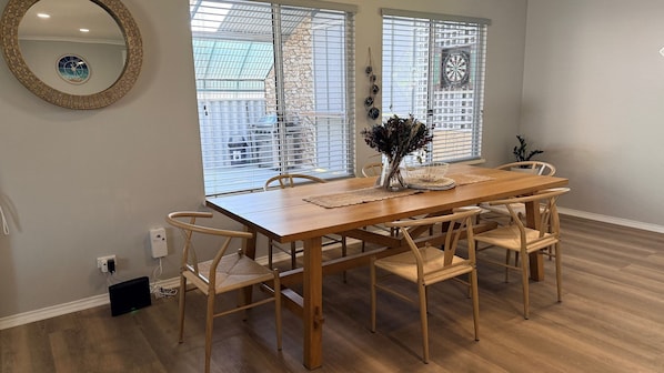 A dining area with a wooden table and chairs, a vase with dried flowers, and a dartboard on the wall.