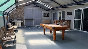 An outdoor pool table with chairs, a grill, and a stone wall.