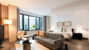 Ein modernes Hotelzimmer mit einer Couch, einem Bett, einem Fernseher und einem großen Fenster.