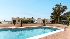 Ein Swimmingpool mit Fliesen umgeben von Gebäuden im mediterranen Stil, Palmen und blauem Himmel.