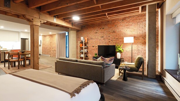 Een kamer met een bed, een bank, een televisie en een bakstenen muur.
