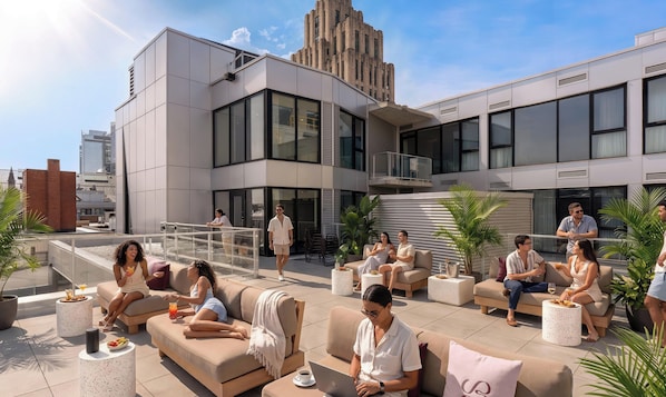 Un salon sur le toit avec des sièges en plein air, un bâtiment moderne en arrière-plan et un ciel dégagé.