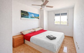 A bedroom with a bed, a nightstand, a ceiling fan, a window, and a painting on the wall.