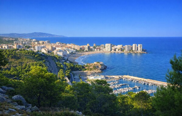 A coastal cityscape with a marina, buildings, and a clear blue sky.