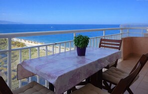 A balcony with a table, chairs, and a potted plant, overlooking a coastal view.