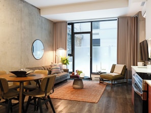A modern living room with a sofa, dining table, chairs, a coffee table, and a large window with curtains. - Loft with Terrace | Serviced Apartment Old Montreal, Courtyard View (Montréal)