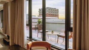 Habitación de hotel con amplias ventanas, vistas a la ciudad, un balcón con mobiliario exterior y una decoración de diseño moderno.