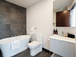 Een moderne badkamer met een vrijstaand bad, toilet en een wastafel met spiegel.
