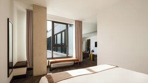 Una habitación de hotel moderna con una cama grande, un banco, un ventanal con vistas y un espejo.