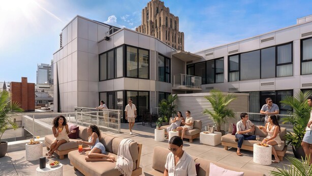 Un lounge en la azotea con mesas al aire libre, un edificio moderno al fondo y un cielo despejado.