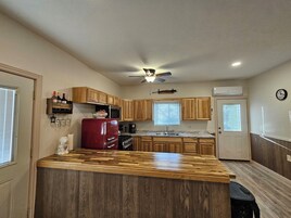 Una cocina compacta con armarios de madera, un refrigerador rojo, un microondas, una cafetera y un ventilador de techo.