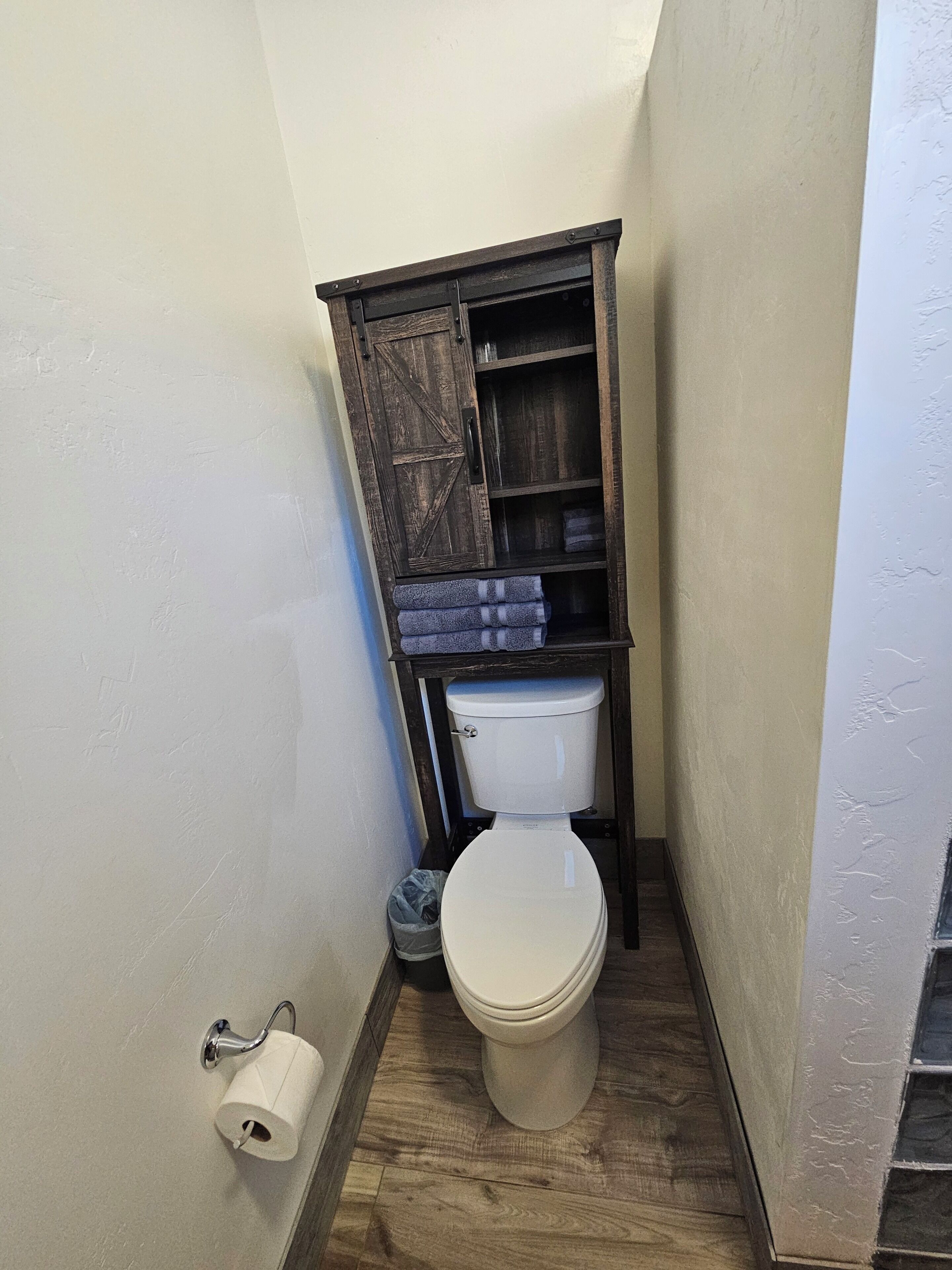 A bathroom with a toilet, wooden cabinet, and a roll of toilet paper.