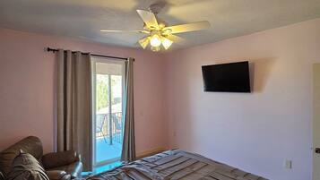 A bedroom with a bed, a ceiling fan, a TV on the wall, and a window with curtains.