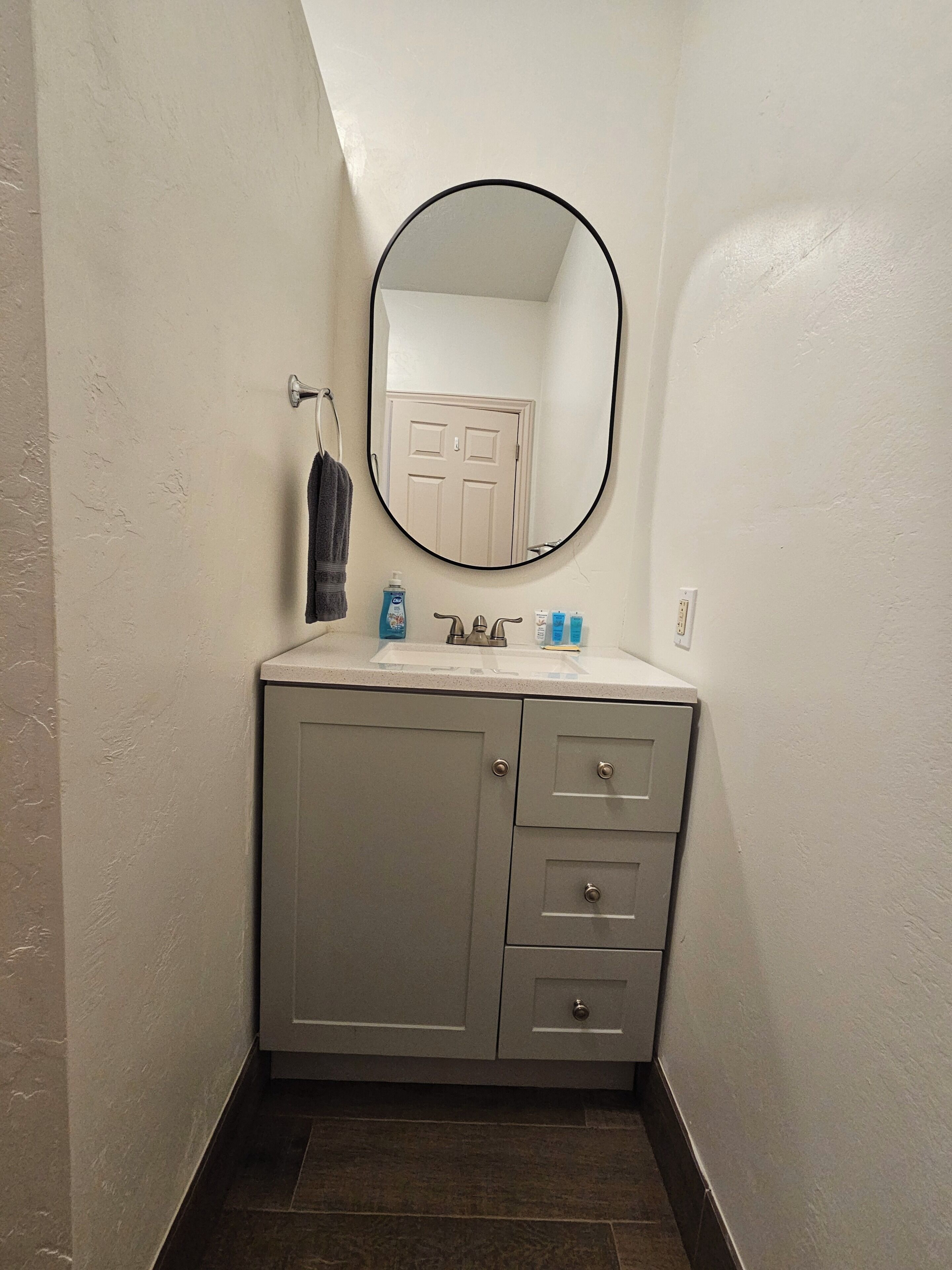 A bathroom with a white vanity, a round mirror, and a towel hanging on the wall.