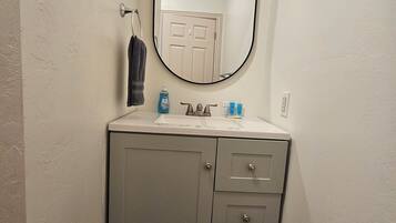 A bathroom with a white vanity, a round mirror, and a towel hanging on the wall.