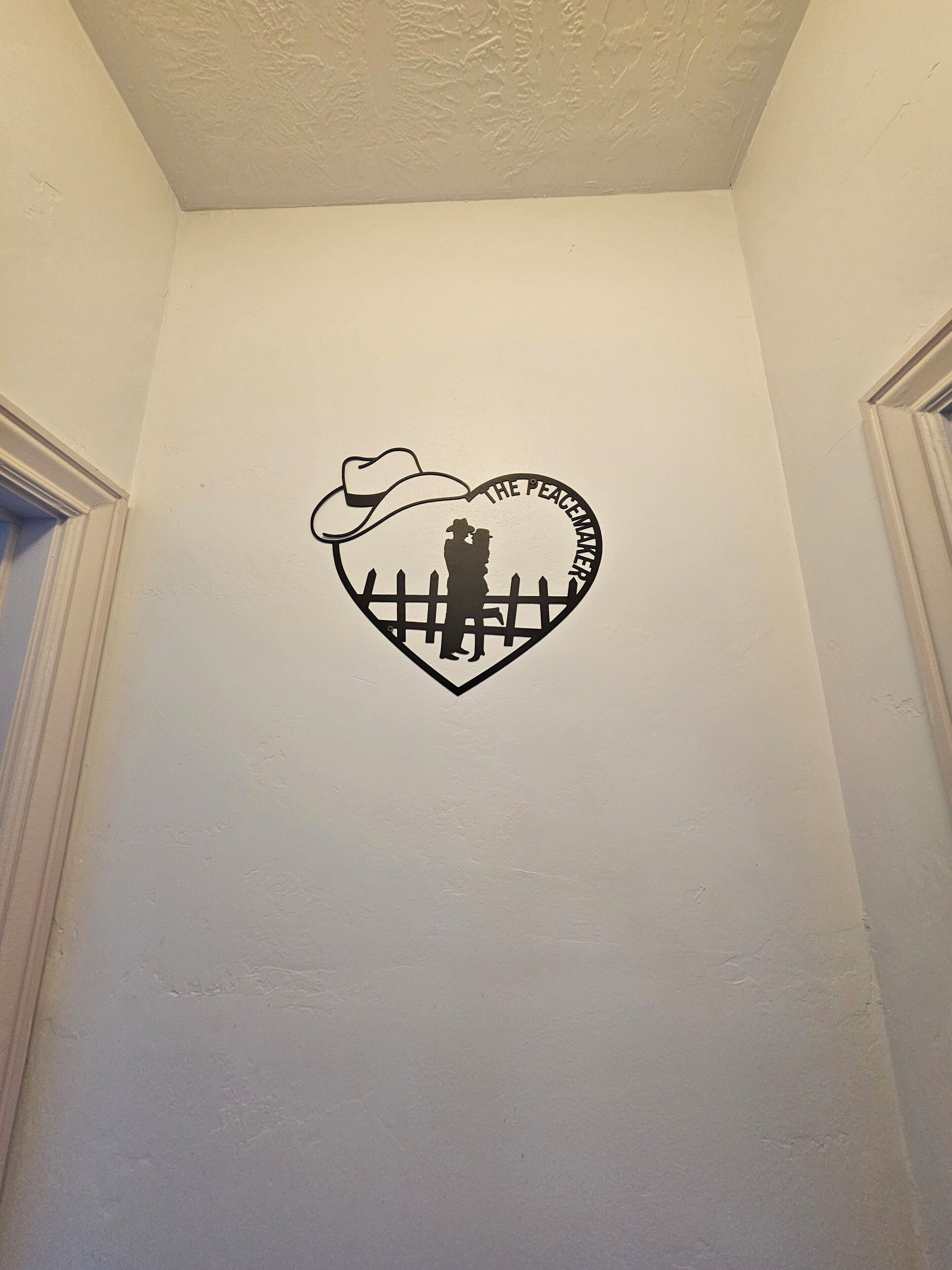 A wall with a heart-shaped cutout featuring a cowboy silhouette and the text 'THE PEACEMAKER.'