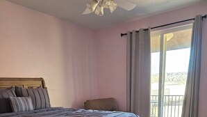Een slaapkamer met een bed, een houten dressoir, een plafondventilator en uitzicht door een raam.