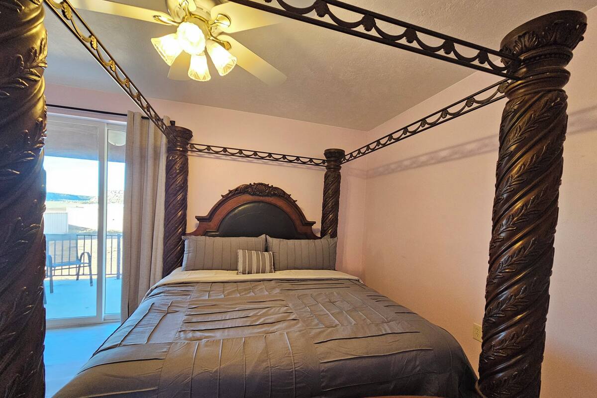 A four-poster bed with a headboard, a ceiling fan, and a balcony view.
