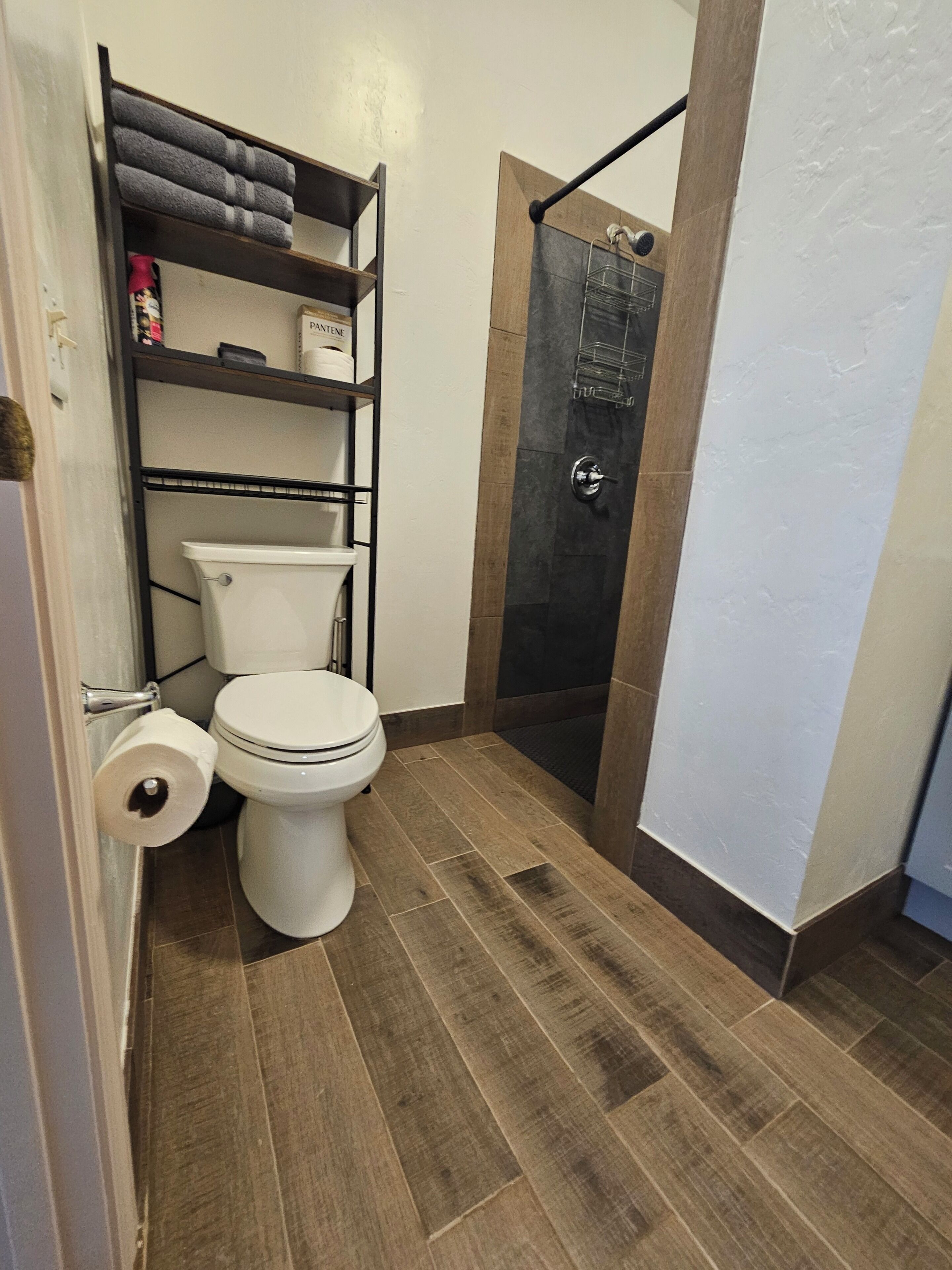 A compact bathroom with a toilet, a shelf with toiletries, and a shower area.