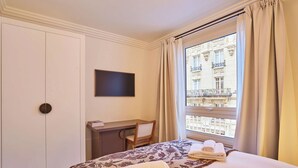 Ein Hotelzimmer mit Bett, Schreibtisch, Stuhl, Fernseher und einem Fenster mit Blick auf ein Gebäude.