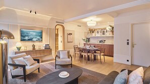 Ein modernes Wohnzimmer mit einer Couch, Sesseln, einem Couchtisch und einem Essbereich mit einer Chandelüster.