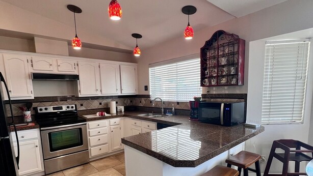 A modern kitchen with white cabinets, a central island, and pendant lighting. - Mesa Nomad Mecca refreshing Diving Pool + splash pad & patio, Dog friendly! (Mesa)